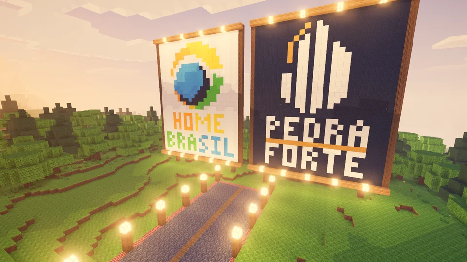 Outdoor gigante feito de blocos coloridos com os símbolos da HomeBrasil e da Pedra Forte, sobre uma praça iluminada por luminárias, em meio a colinas verdes e pinheiros ao entardecer.